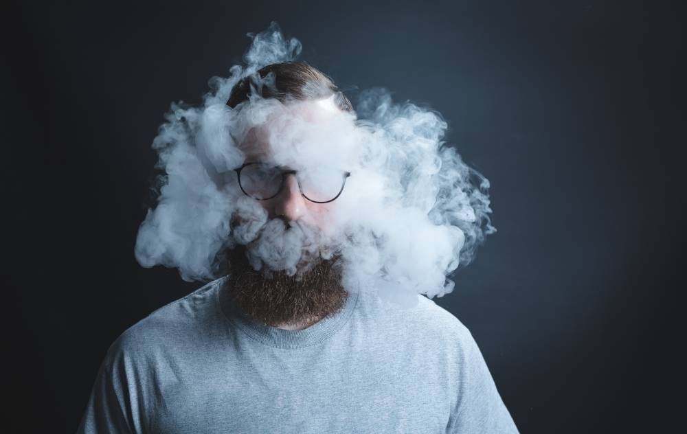 Man clouded by secondhand smoke against dark background