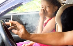 Child in car closing nose as parent smokes as they drive