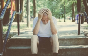 Older man sitting on steps outside depressed