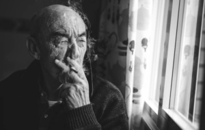 Old man in black and white smokes by window