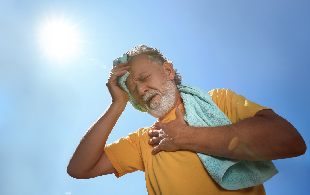 Older white man is patting his head with a towel and holding onto his chest due to dehydration.