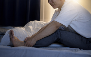 Man wakes up at night with intense leg pain and grabs his leg, possibly from peripheral artery disease and sleep apnea.