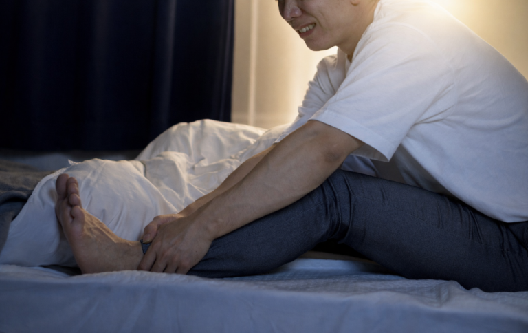 Man wakes up at night with intense leg pain and grabs his leg, possibly from peripheral artery disease and sleep apnea.